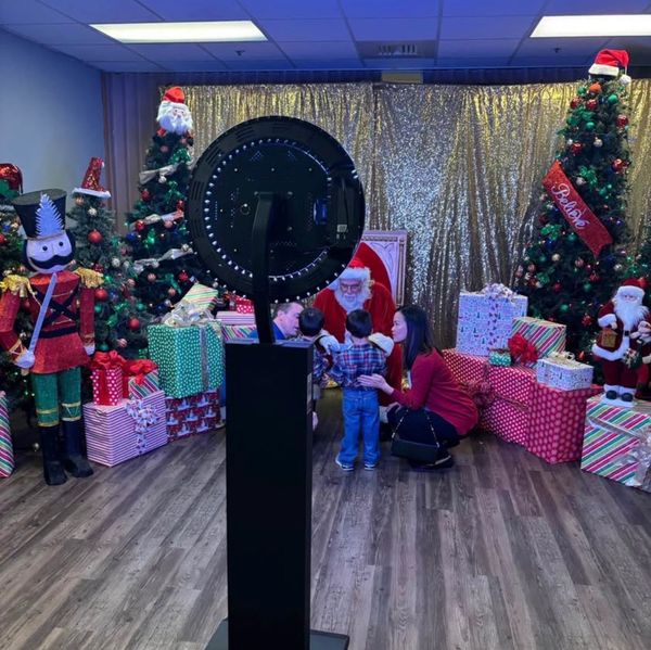 Children meet Santa surrounded by Christmas trees, gifts, and holiday decorations.