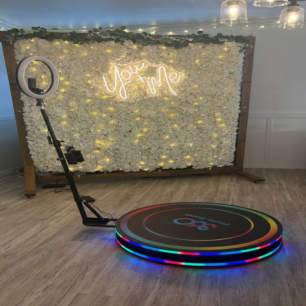 Photo booth setup with floral backdrop and neon sign.