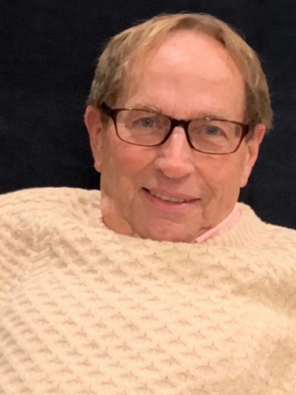 Smiling elderly man wearing glasses and a cream-colored sweater.
