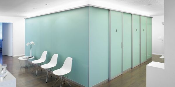 Modern waiting area with white chairs and glass doors labeled A, B, C.