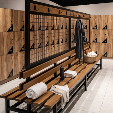 Modern locker room with wooden lockers and a bench with towels and a robe.