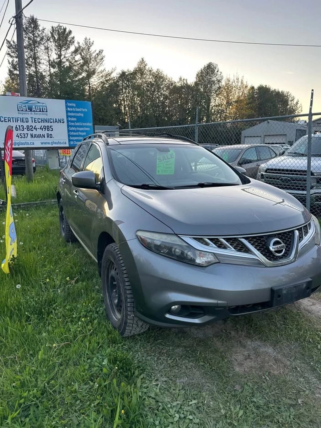 Gray Nissan SUV parked on grass with sale sign inside.