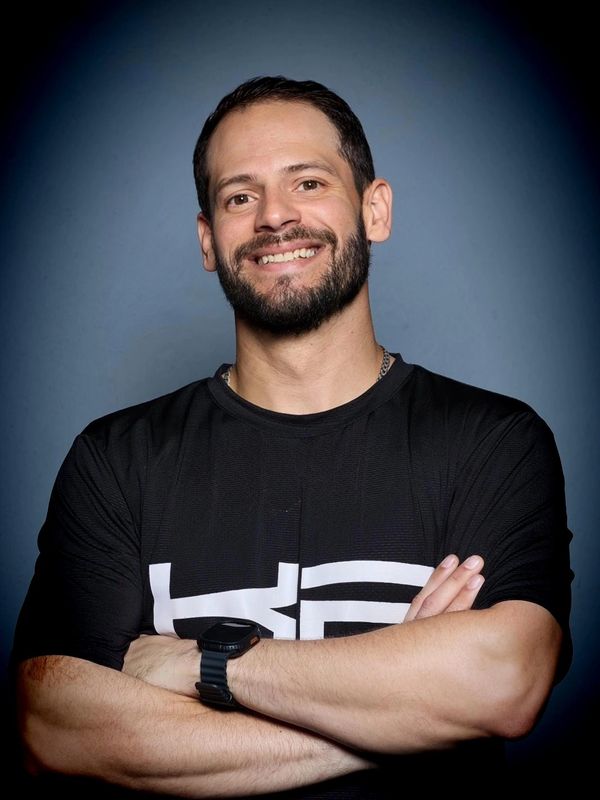 Smiling man with beard and crossed arms wearing a black t-shirt and watch.