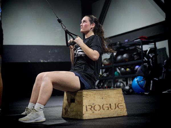 Woman performing cable row exercise sitting on a wooden box in a gym.