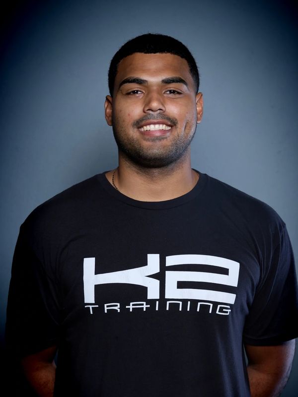 Smiling man wearing a black K2 Training t-shirt against a blue background.