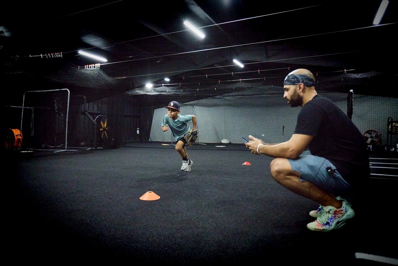 A boy runs between cones while an adult coaches him indoors.