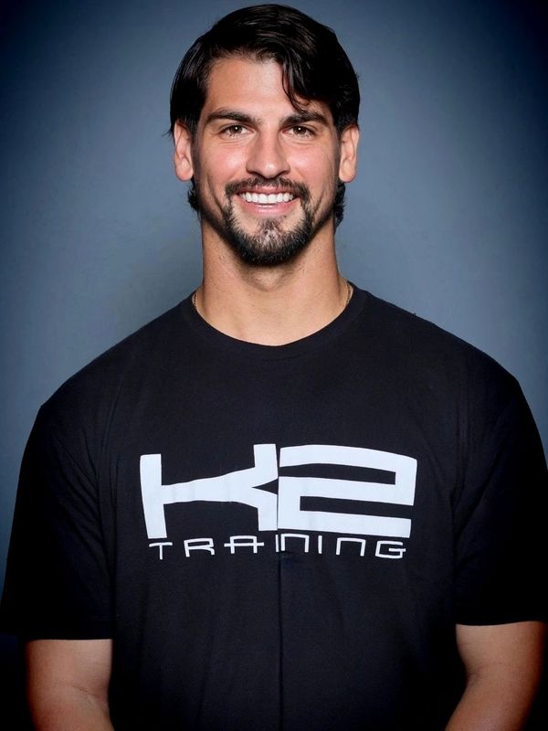 Smiling man in a black K2 Training t-shirt against a dark background.