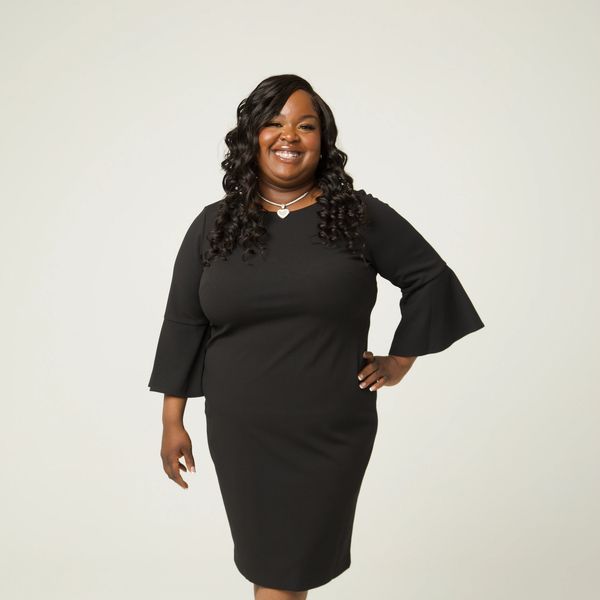 Confident woman in a black dress smiling against a plain background.