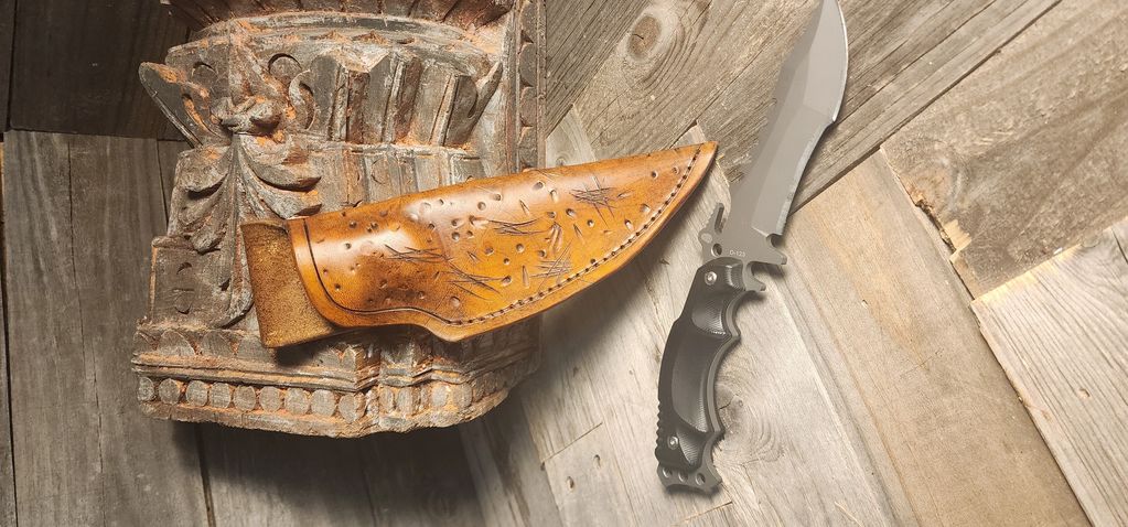 Cuchillo con funda de cuero sobre una superficie de madera y piedra tallada.