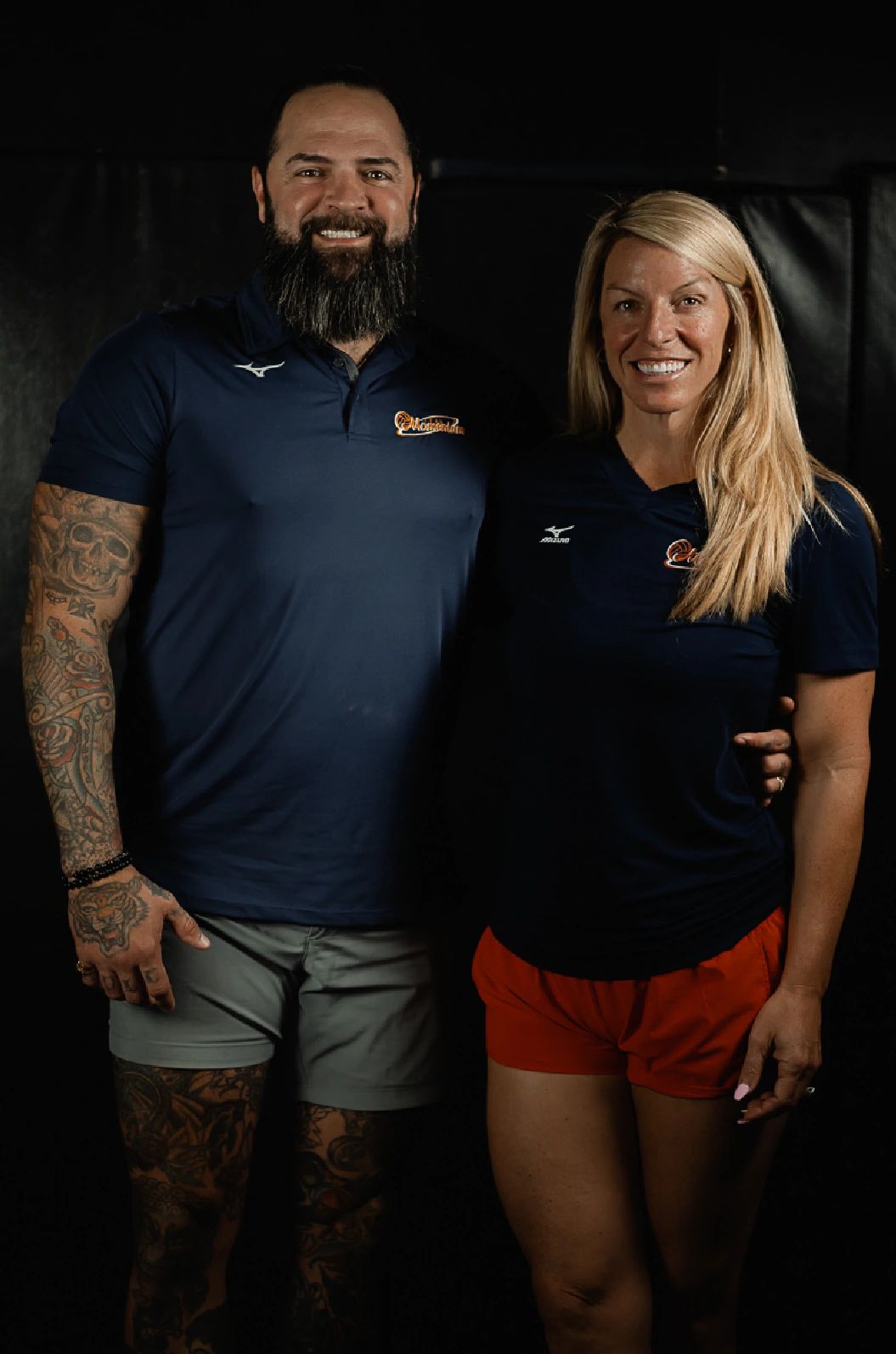 Smiling tattooed man and blonde woman in sportswear pose together.
