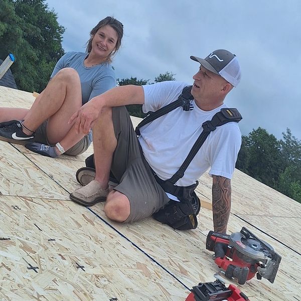 Two people taking a break on a wooden roof under construction with power tools nearby.