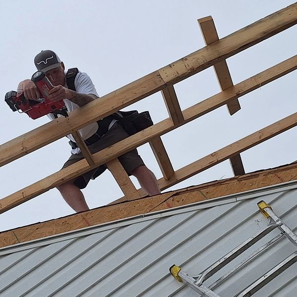 Construction worker using a nail gun on a roof frame.