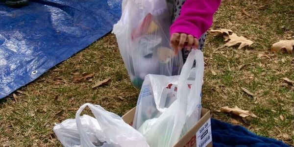 A person sorting plastic bags filled with recyclables outdoors on grass.