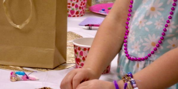 Child wearing colorful beads and bracelets at a decorated party table.