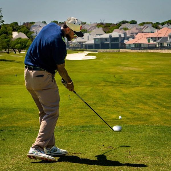 Man in blue shirt teeing off on a sunny golf course.