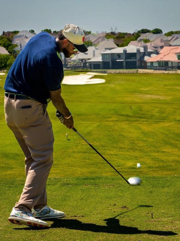 Man in blue shirt teeing off on a sunny golf course.