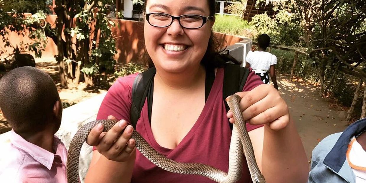 Sarah at a reptile zoo in Tanzania. She is holding a snake in her hands with a big smile.
