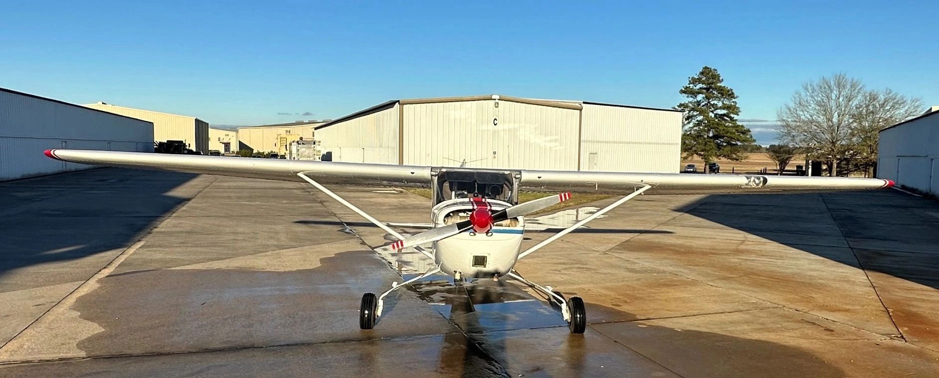 Small single-engine airplane parked on a concrete airstrip near hangars.