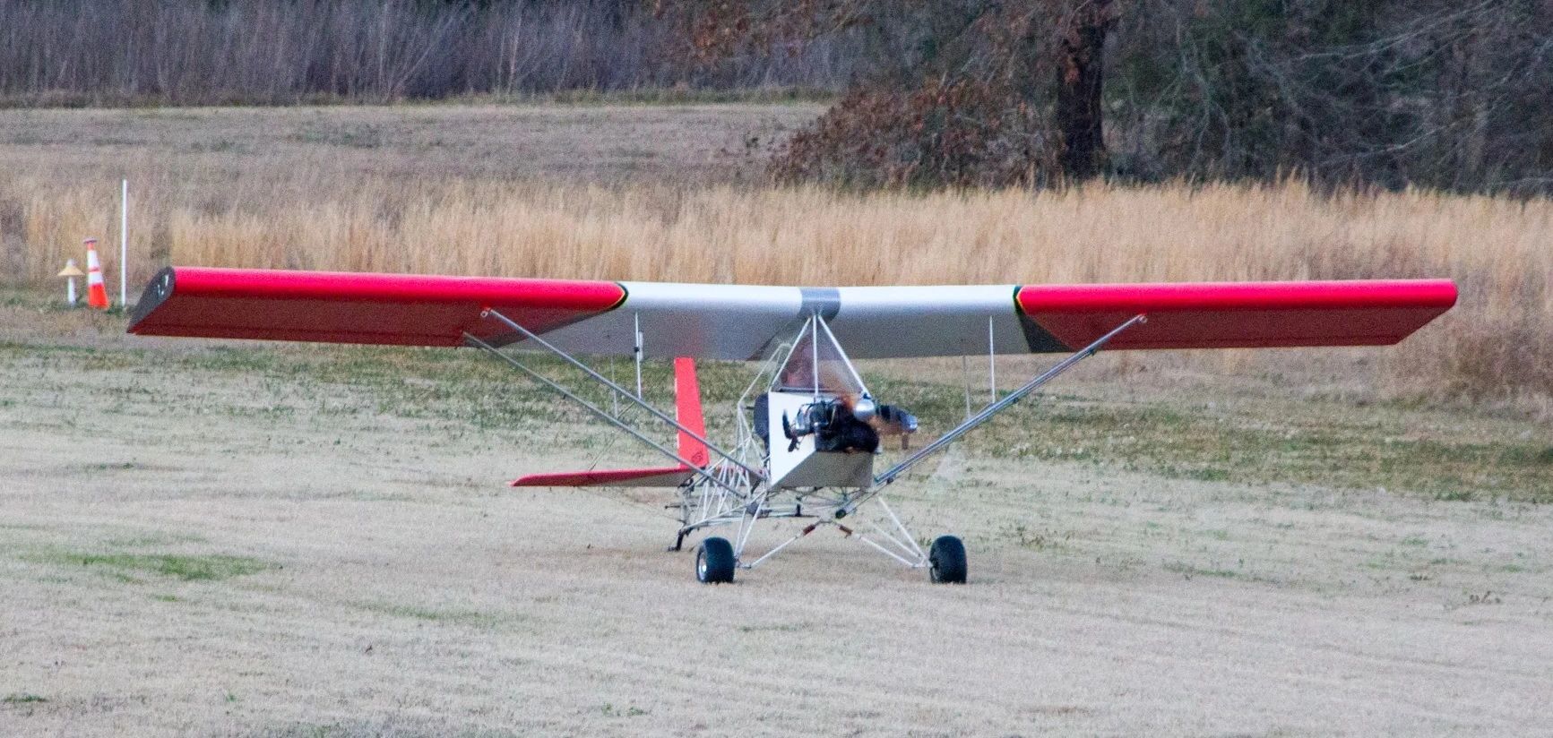 Small ultralight airplane on grass runway with red-tipped wings.