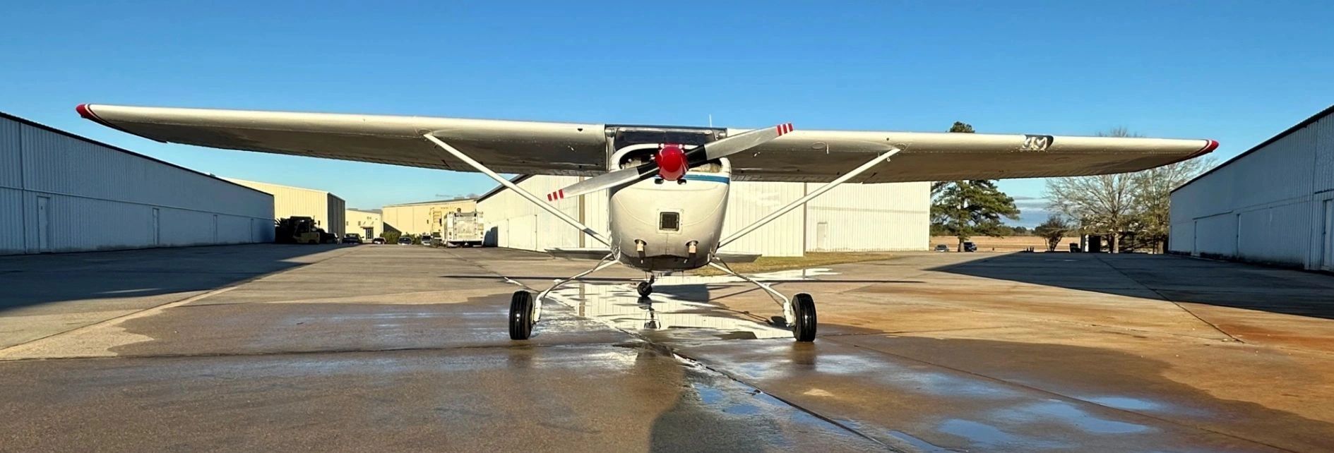 Front view of a small white airplane parked on a wet runway.