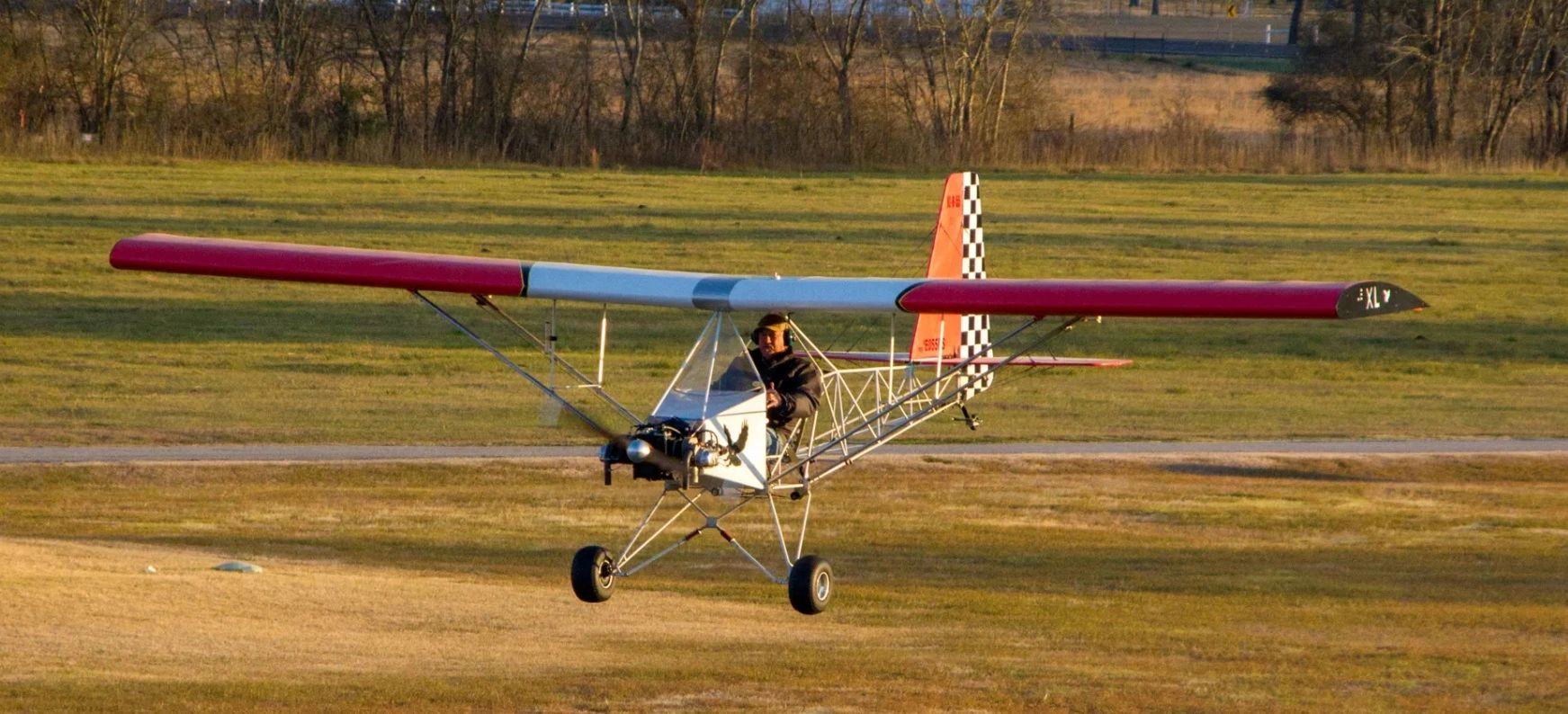 A small ultralight aircraft flying low over a grassy field.