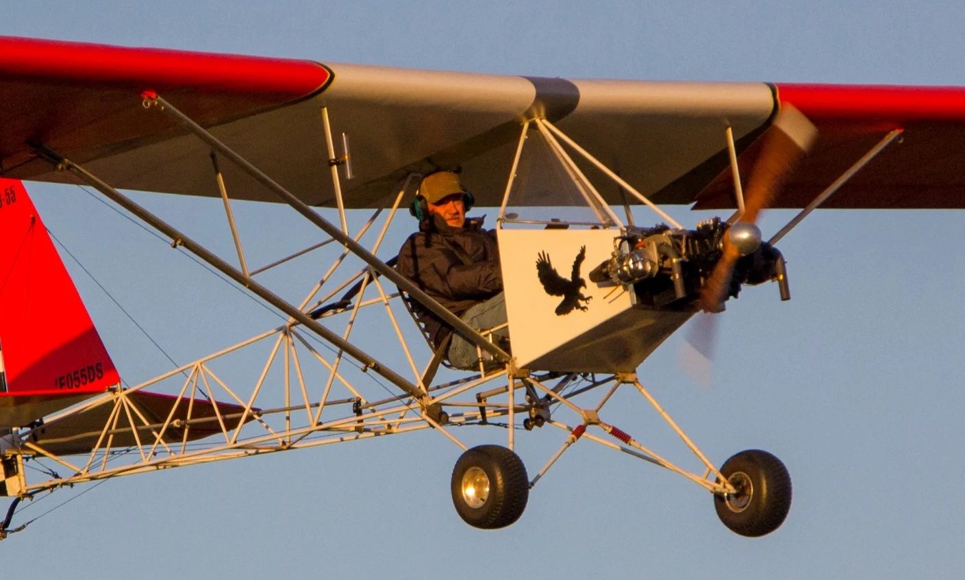 A man piloting a lightweight ultralight aircraft with a red and white wing.