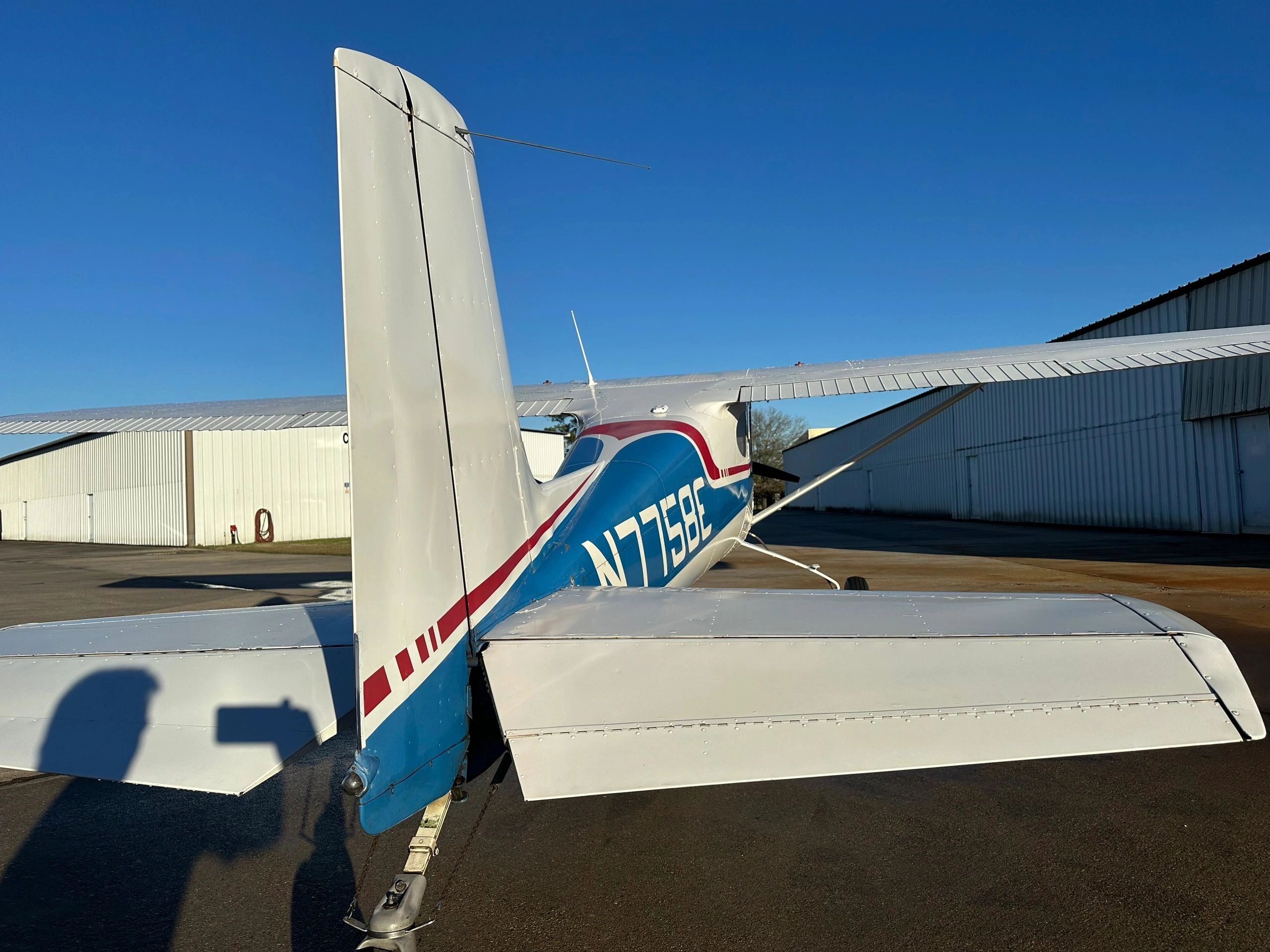 Rear view of a small airplane with blue, white, and red markings on the tarmac.