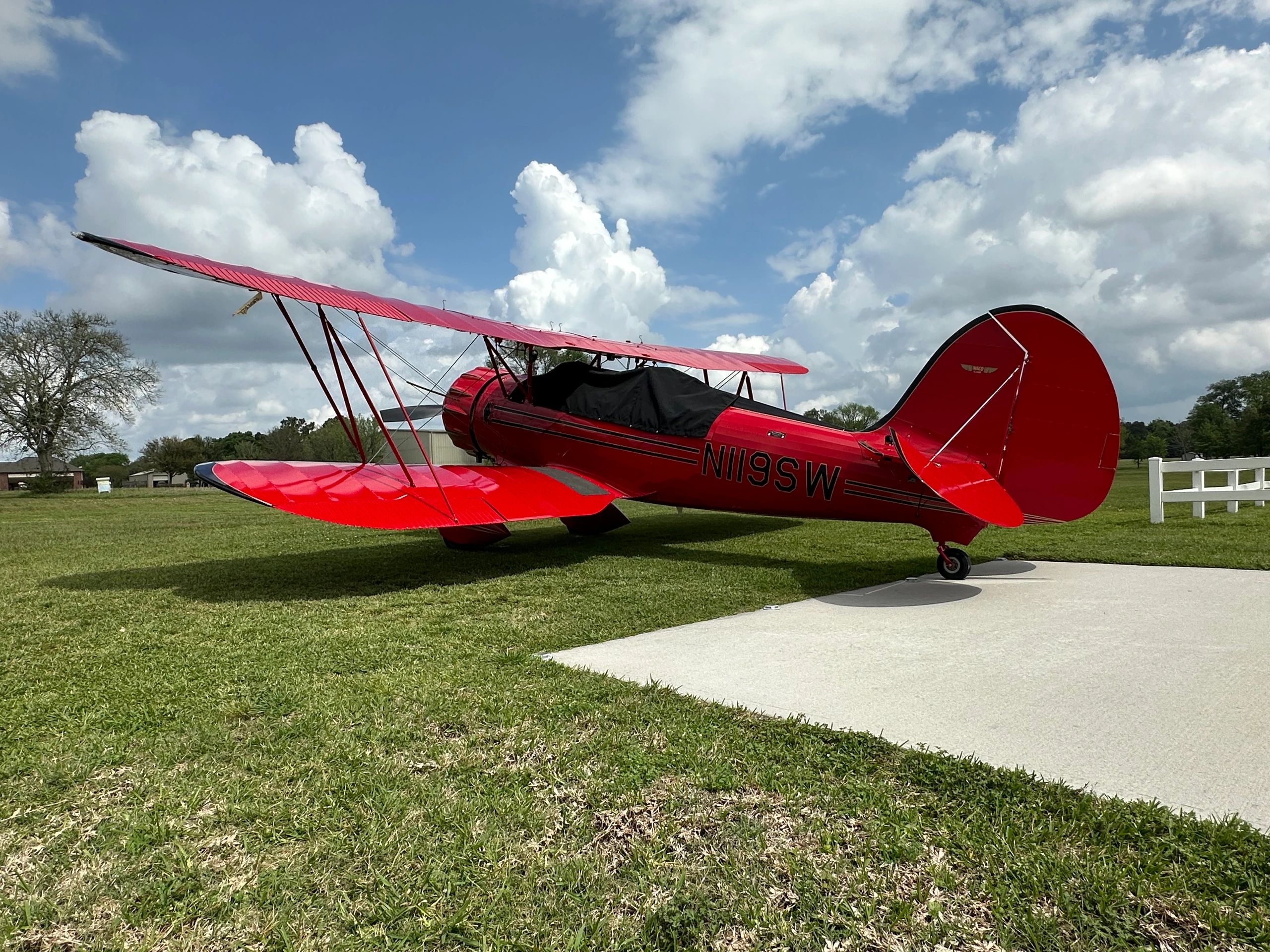 A bright red vintage biplane parked on grass under a partly cloudy sky.