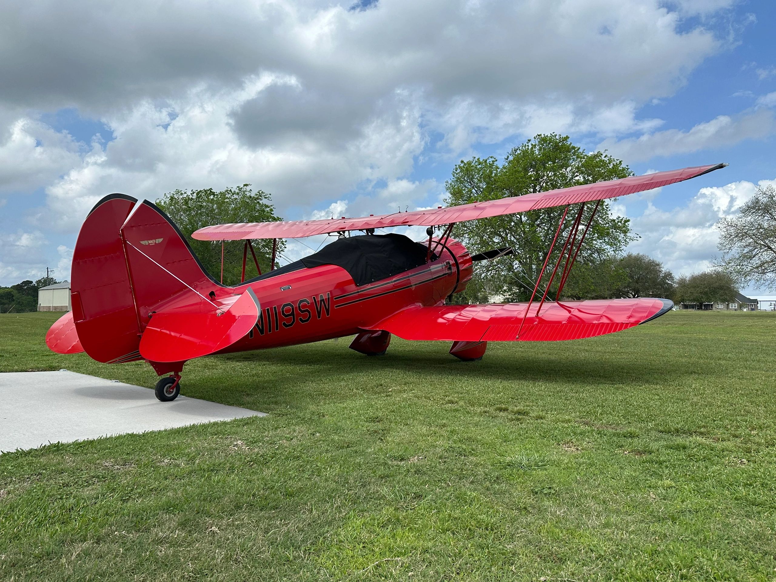 A bright red vintage biplane on grass under a cloudy sky.