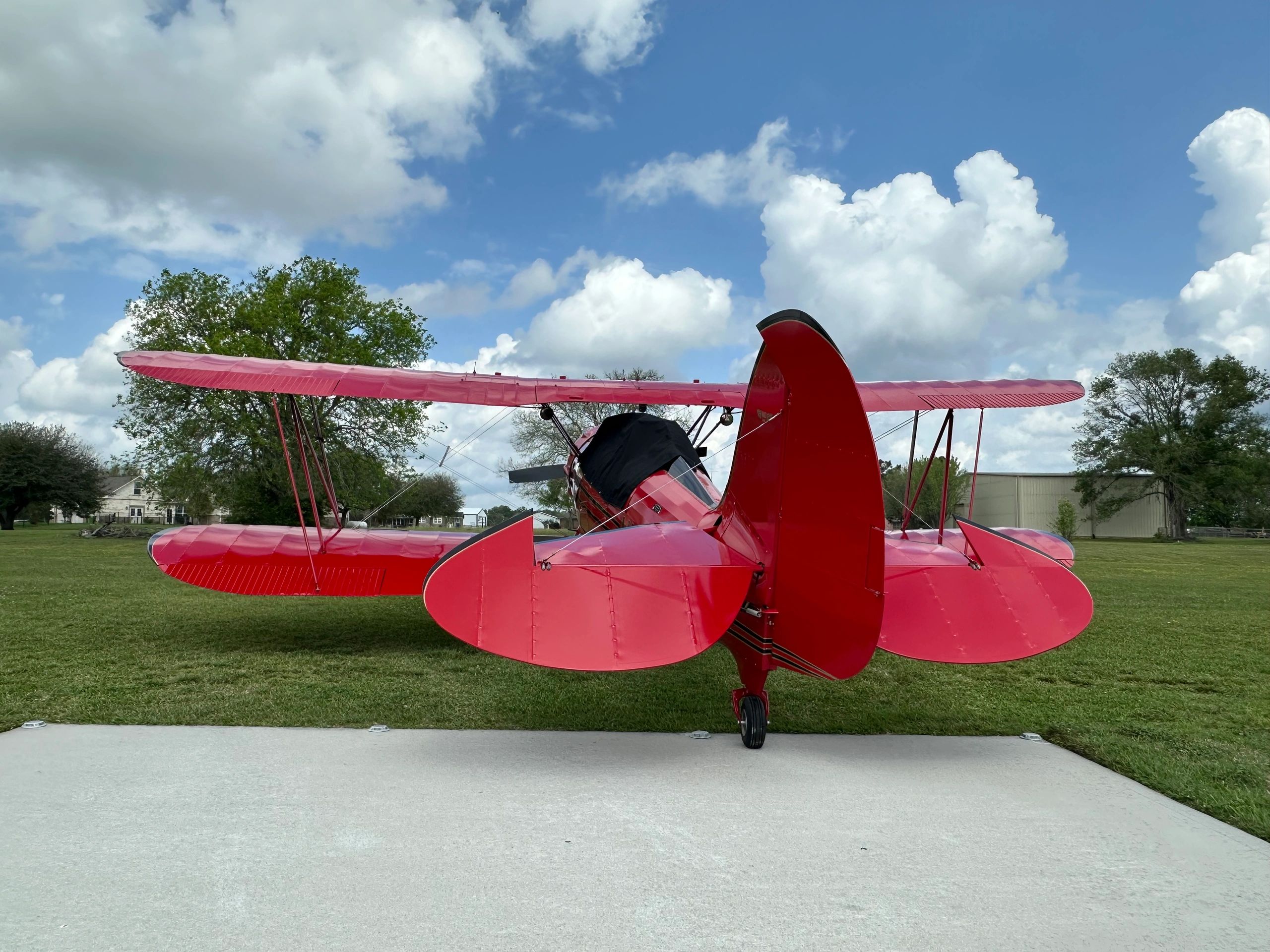 Red vintage biplane parked on grass with blue sky.
