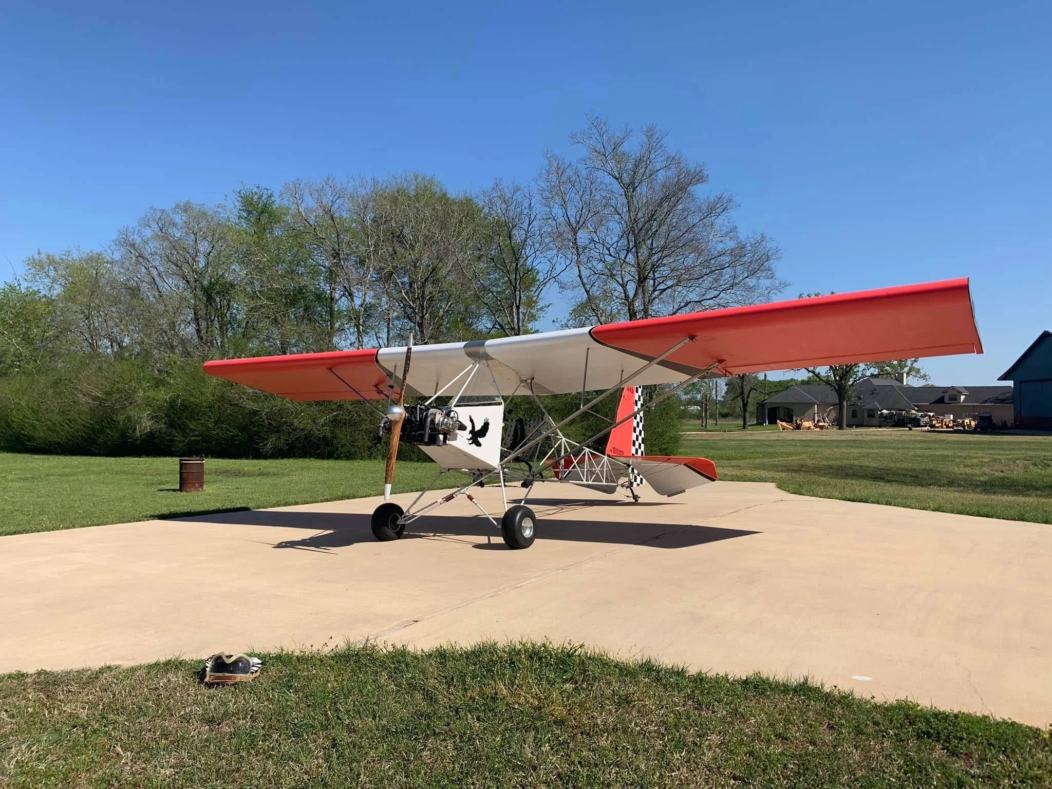 A small, lightweight airplane with red and white wings parked on a concrete pad.