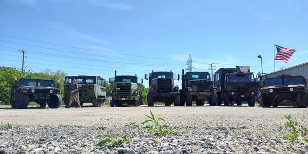 A lineup of military vehicles under a clear blue sky with an American flag.