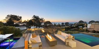 Modern outdoor lounge with fire pit and pool overlooking a scenic sunset.