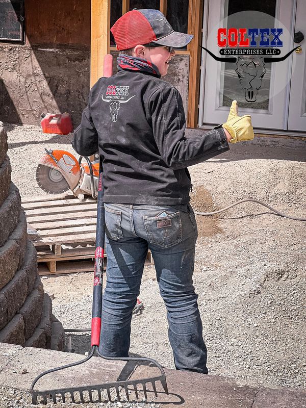 Young worker giving thumbs up at construction site holding a rake.