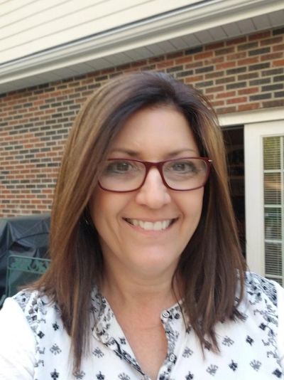 Woman smiling outdoors with glasses and brown hair.