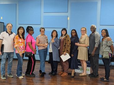 A diverse group of nine people standing in a row indoors, smiling.
