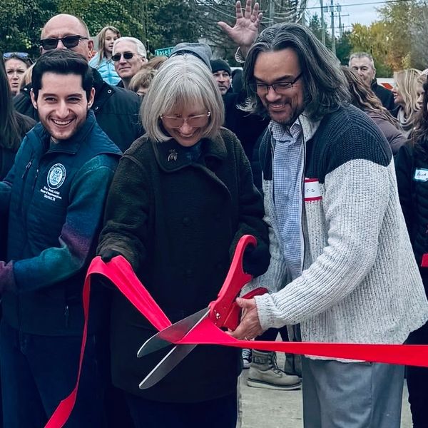 People smiling and cutting a red ribbon at an outdoor event.