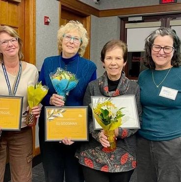 Four women holding awards and flowers, smiling.
