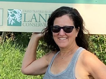 Smiling woman in sunglasses poses by a nature conservation sign outdoors.