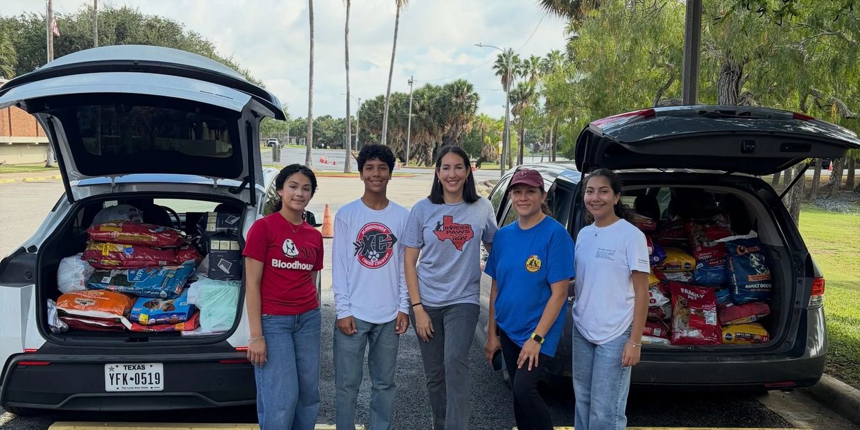 Group of five people standing between two cars loaded with dog food.