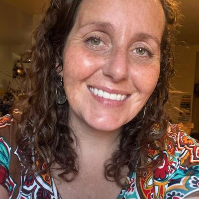 Smiling woman with curly hair and patterned shirt.