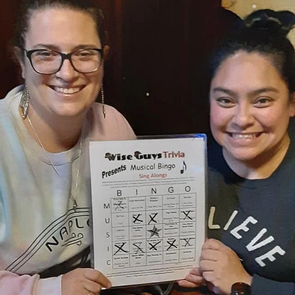 Two women smiling and holding a musical bingo score sheet.
