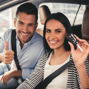 Happy couple in a car showing car keys and thumbs up.