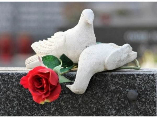 Two white dove sculptures with a red rose on a dark granite surface.