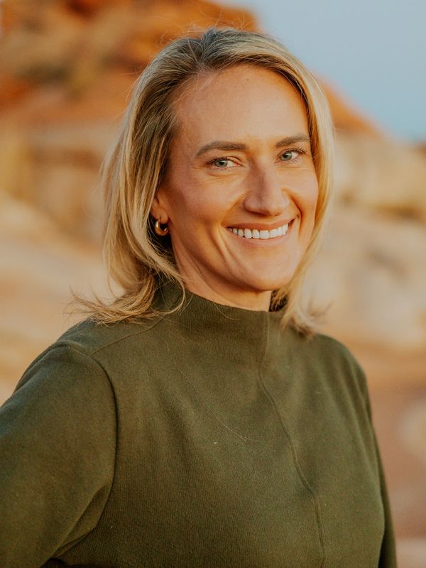 Smiling woman in green sweater outdoors with a rocky background.