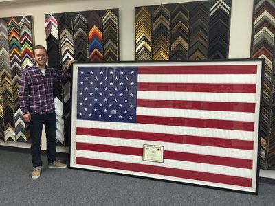 Man standing next to a large framed American flag with a certificate inside.