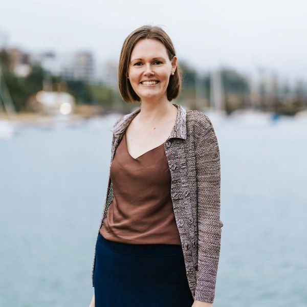 Smiling woman standing near a waterfront with boats in the background.
