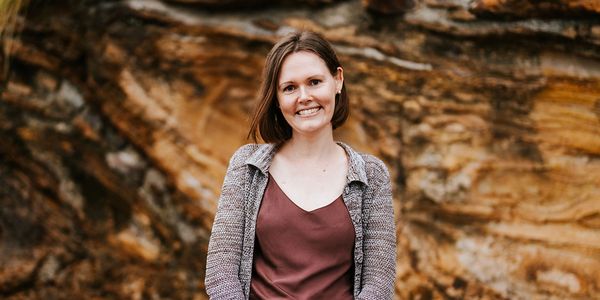 Smiling woman standing outdoors against a rocky background.