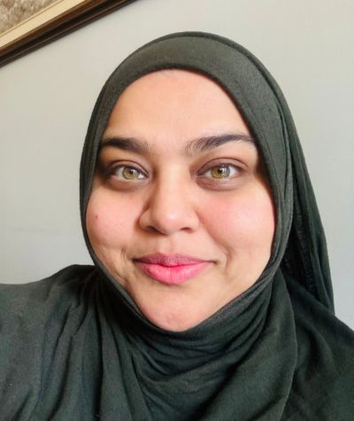 Close-up of a woman wearing a dark green hijab and smiling gently.