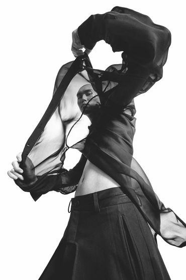 Black-and-white photo of a person wearing a flowing sheer black blouse and a skirt.